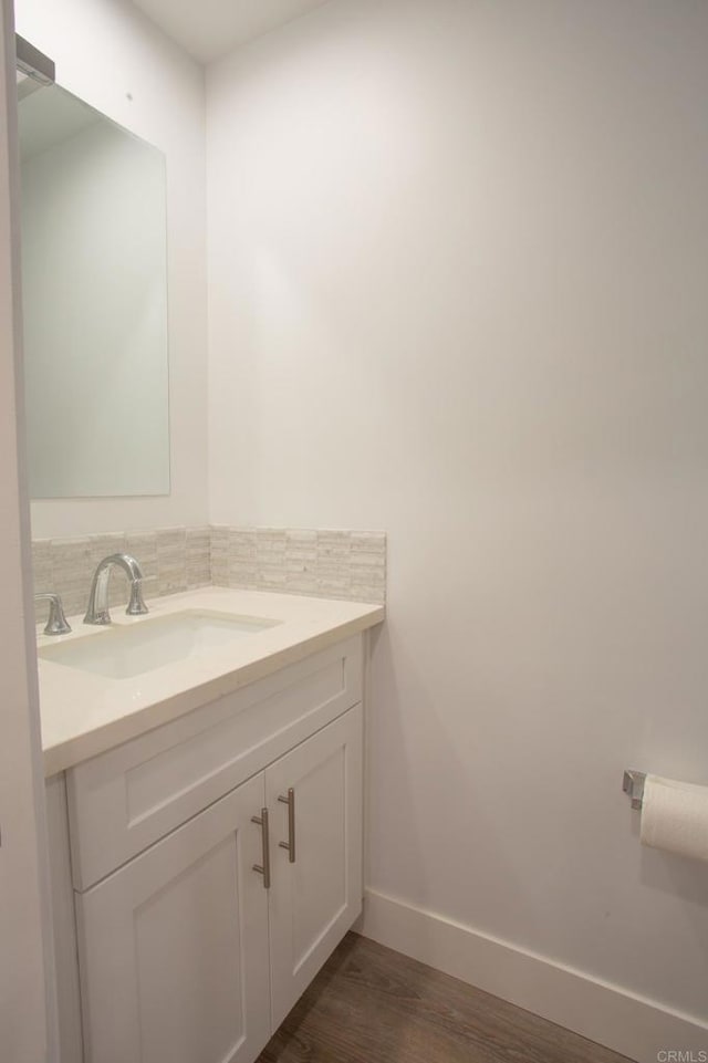 bathroom with baseboards, decorative backsplash, vanity, and wood finished floors