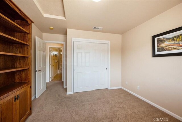 unfurnished bedroom featuring light carpet, attic access, baseboards, visible vents, and a closet