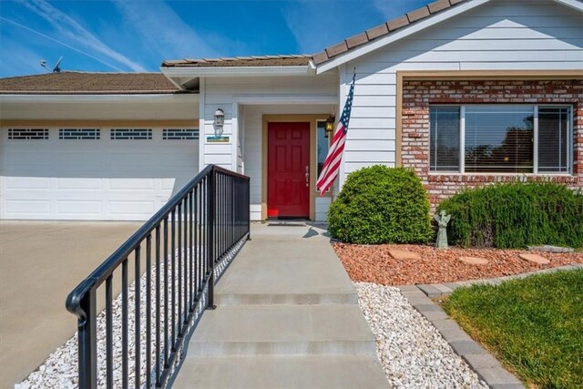 doorway to property with a garage, driveway, a tile roof, and brick siding