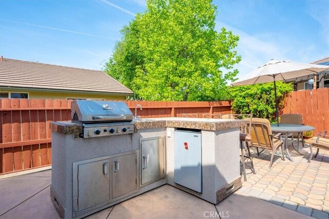 view of patio featuring outdoor dry bar, exterior kitchen, area for grilling, a fenced backyard, and a sink