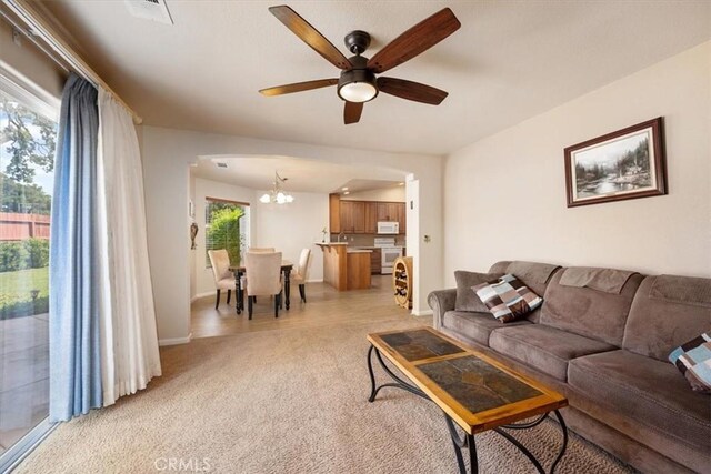 living area featuring baseboards, arched walkways, ceiling fan with notable chandelier, and light carpet