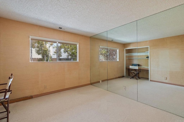interior space with a textured ceiling, visible vents, baseboards, and carpet