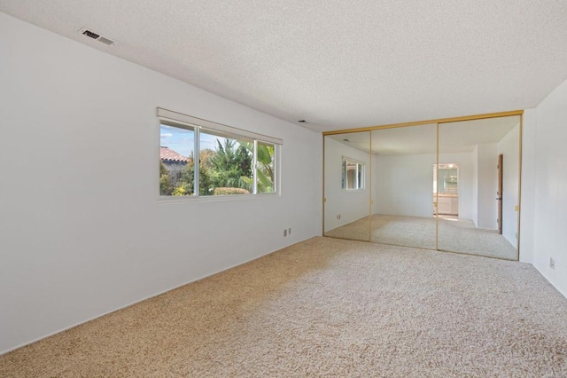 spare room with carpet floors, a textured ceiling, and visible vents