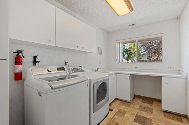 laundry area with a textured ceiling, visible vents, washing machine and dryer, cabinet space, and a sink
