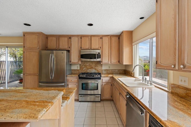 kitchen with a sink, a textured ceiling, appliances with stainless steel finishes, and light tile patterned floors
