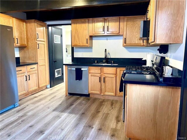 kitchen with dark countertops, appliances with stainless steel finishes, a sink, and light wood-type flooring