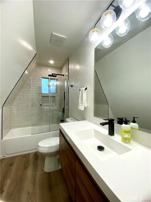 full bathroom featuring vanity, toilet, combined bath / shower with glass door, wood finished floors, and visible vents