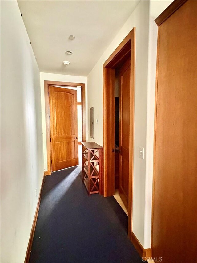 hallway featuring baseboards and dark colored carpet