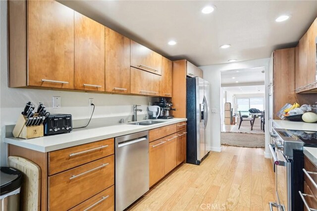 kitchen featuring recessed lighting, light countertops, a sink, light wood finished floors, and appliances with stainless steel finishes