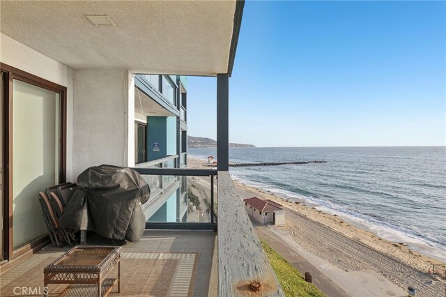 balcony with a water view, a view of the beach, and a grill