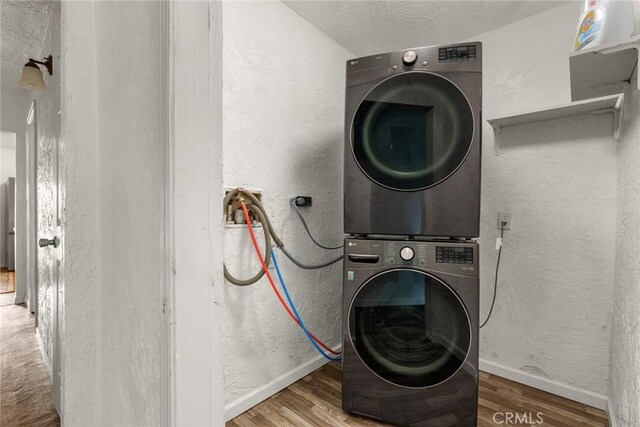clothes washing area featuring baseboards, laundry area, wood finished floors, and stacked washer and clothes dryer