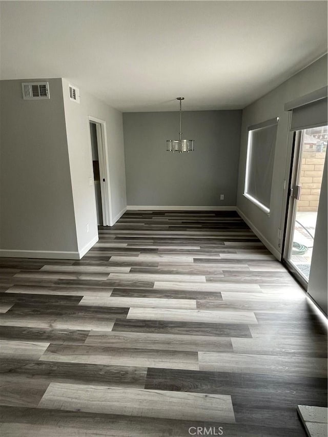 unfurnished dining area with a chandelier, baseboards, visible vents, and wood finished floors