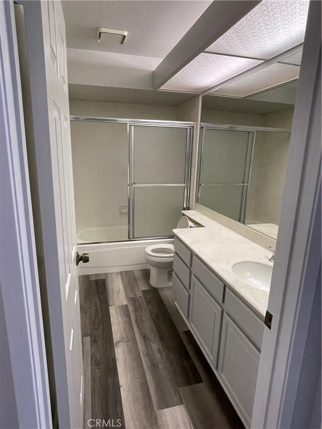 bathroom featuring shower / bath combination with glass door, vanity, toilet, a textured ceiling, and wood finished floors