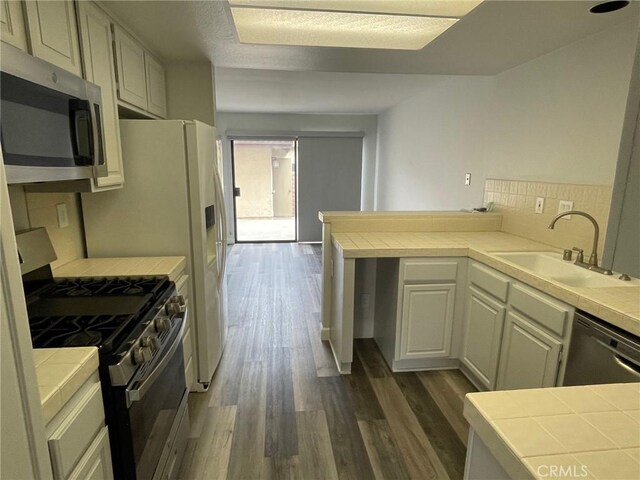 kitchen featuring appliances with stainless steel finishes, a sink, a peninsula, dark wood-style floors, and tile counters