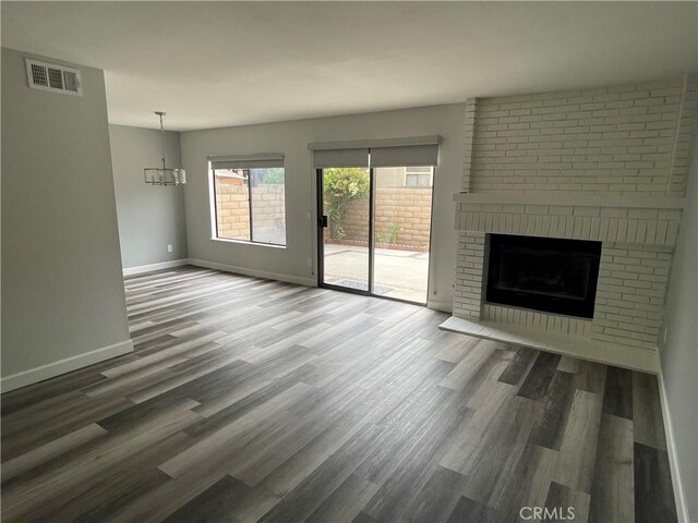 unfurnished living room featuring visible vents, a fireplace, wood finished floors, baseboards, and a chandelier