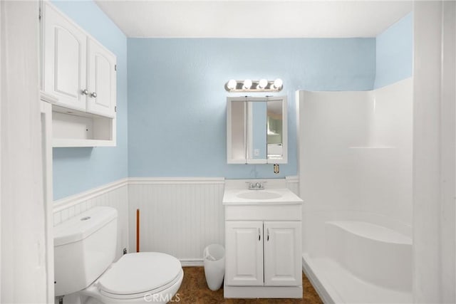 full bathroom featuring vanity, toilet, walk in shower, and a wainscoted wall
