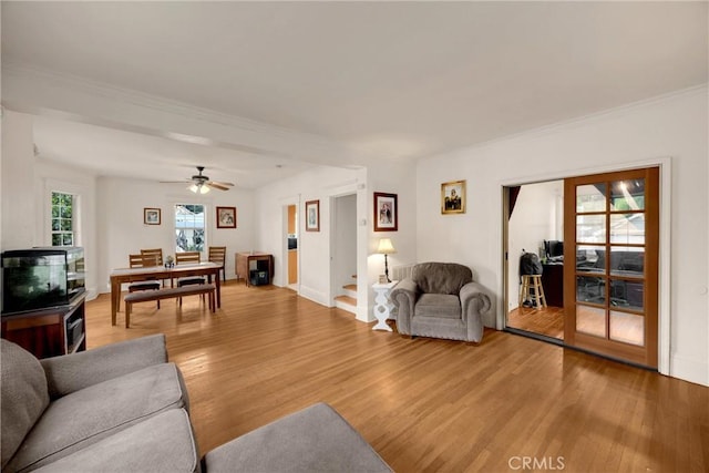 living area with light wood-type flooring, ornamental molding, baseboards, and a ceiling fan