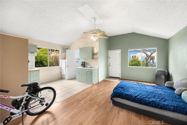 bedroom with ceiling fan, light wood finished floors, a textured ceiling, and lofted ceiling