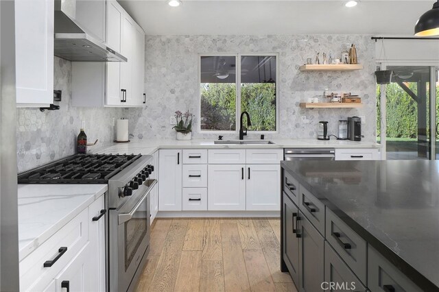 kitchen with light stone countertops, high end stainless steel range, a sink, light wood-style floors, and wall chimney exhaust hood