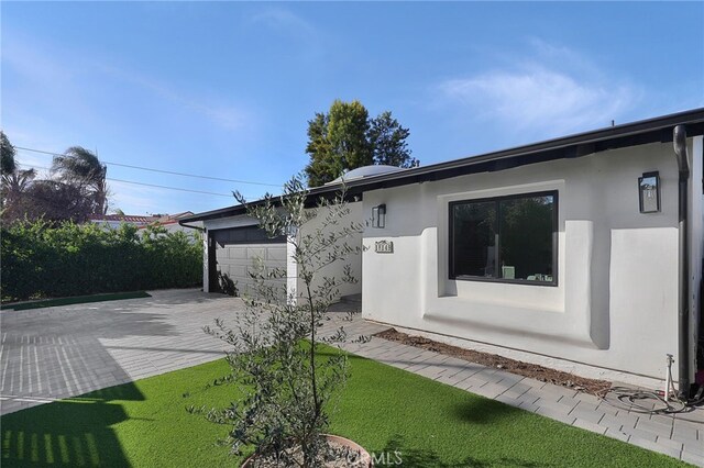 rear view of property with an attached garage, driveway, and stucco siding