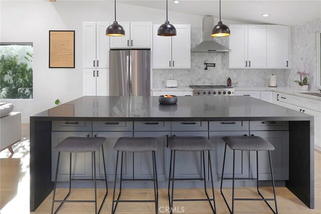 kitchen with freestanding refrigerator, white cabinetry, dark countertops, and wall chimney range hood