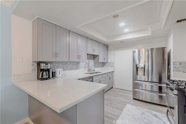kitchen featuring a sink, a peninsula, backsplash, light countertops, and appliances with stainless steel finishes