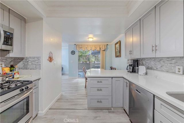 kitchen with a peninsula, ornamental molding, light countertops, and appliances with stainless steel finishes