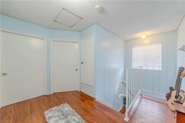 interior space featuring a textured ceiling, attic access, an upstairs landing, and wood finished floors