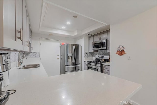 kitchen with a sink, stainless steel appliances, tasteful backsplash, light countertops, and a raised ceiling