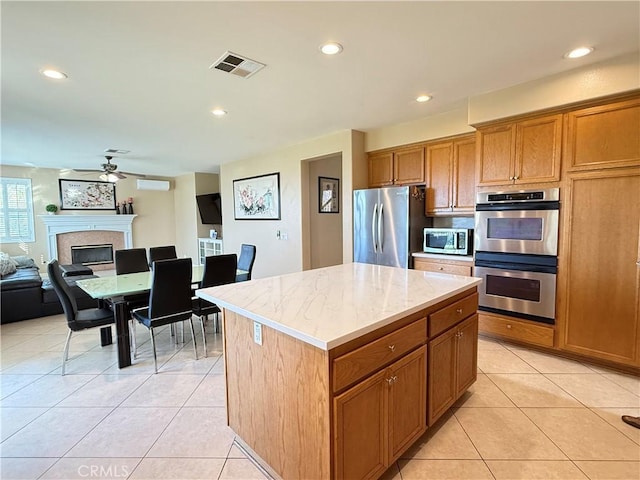12271 Oldenberg Ct, Rancho Cucamonga, CA 91739 - kitchen featuring stainless steel appliances, a ceiling fan, brown cabinetry, a fireplace, and light tile patterned flooring
