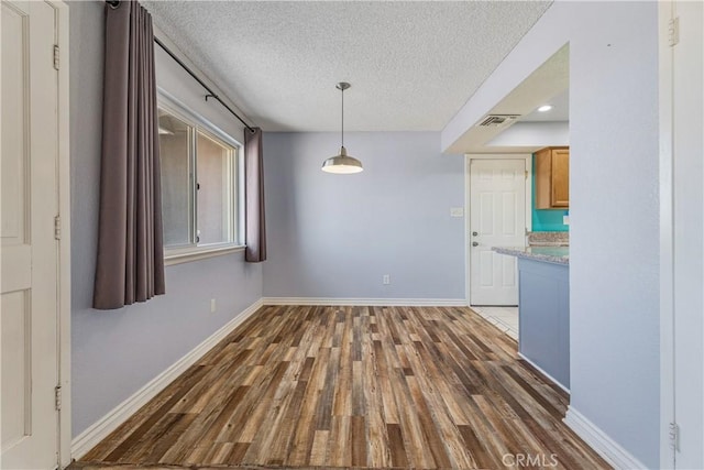 unfurnished dining area featuring baseboards, a textured ceiling, visible vents, and wood finished floors