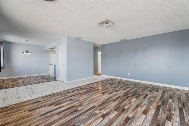 spare room with baseboards, a textured ceiling, visible vents, and wood finished floors