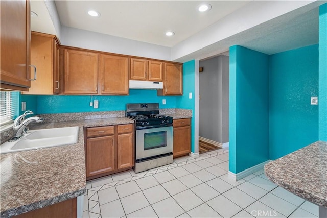 kitchen featuring under cabinet range hood, brown cabinets, a sink, and stainless steel gas range oven