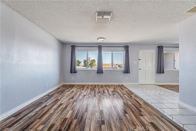 empty room featuring a textured ceiling, visible vents, and wood finished floors