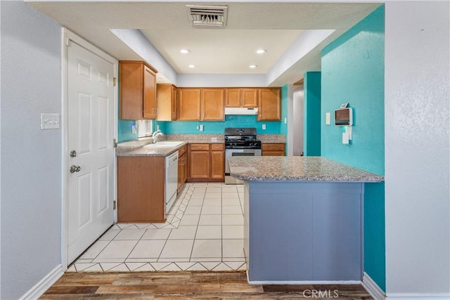 kitchen with white dishwasher, a sink, stainless steel gas stove, under cabinet range hood, and visible vents