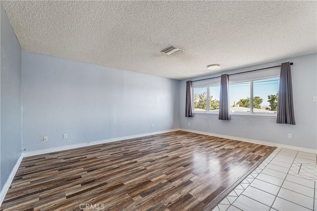 spare room with baseboards, a textured ceiling, wood finished floors, and visible vents