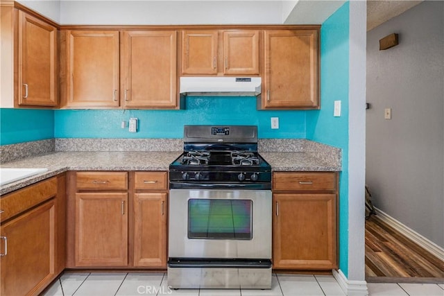 kitchen featuring brown cabinets, light tile patterned flooring, stainless steel gas range oven, baseboards, and under cabinet range hood