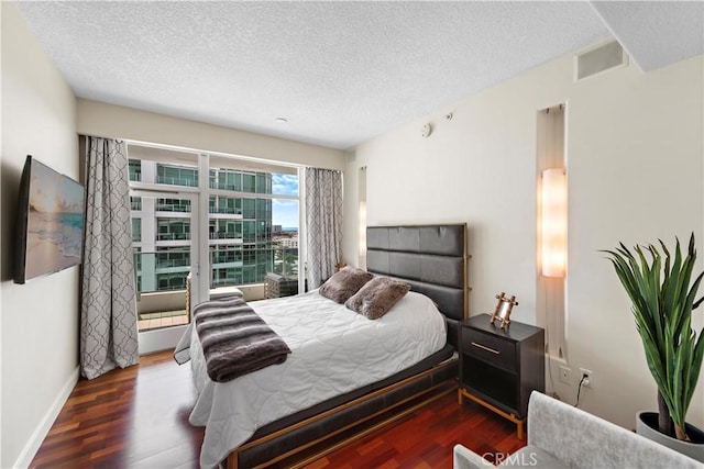 bedroom featuring baseboards, a textured ceiling, visible vents, and wood finished floors