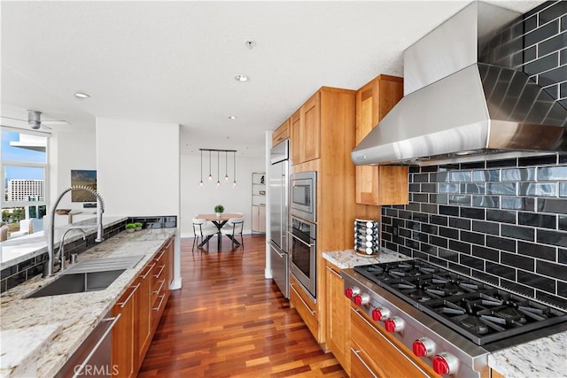 kitchen with built in appliances, dark wood-style floors, wall chimney range hood, a sink, and backsplash