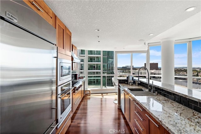 kitchen with brown cabinetry, built in appliances, dark wood-type flooring, a textured ceiling, and a sink