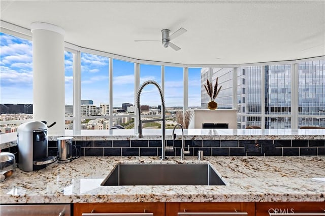 kitchen with a view of city, a ceiling fan, brown cabinets, light stone counters, and a sink