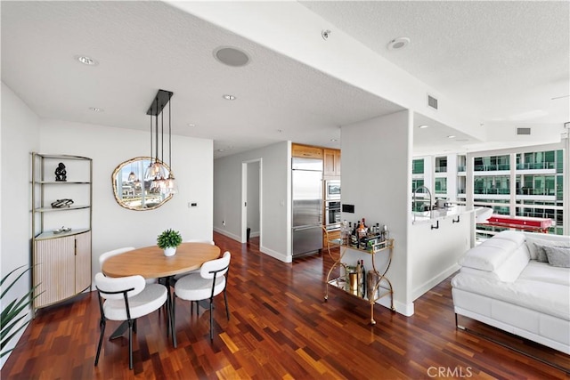 dining room with a textured ceiling, dark wood finished floors, plenty of natural light, and an inviting chandelier