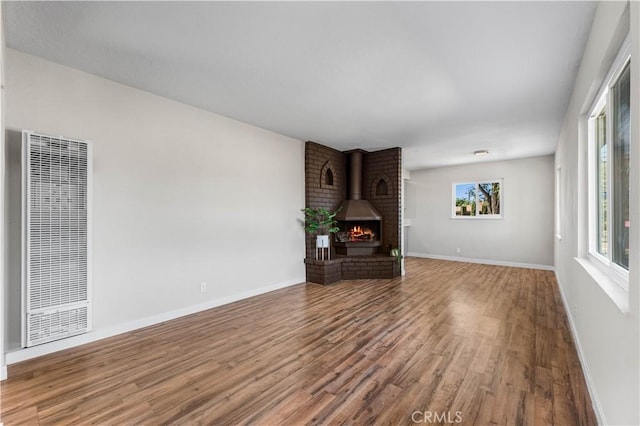 unfurnished living room featuring baseboards, a heating unit, wood finished floors, and a fireplace