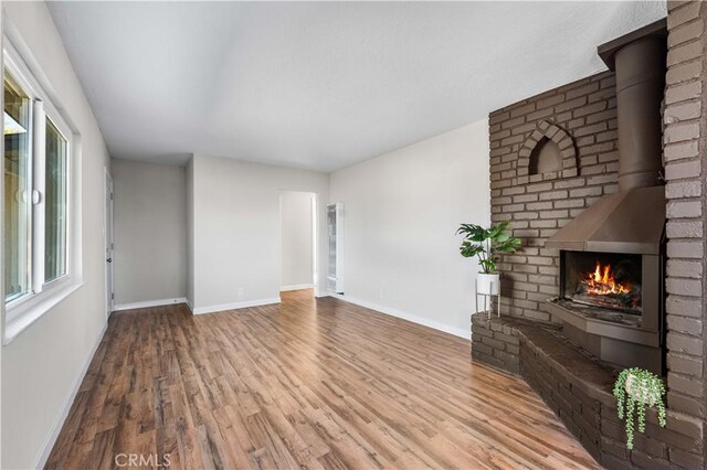 unfurnished living room featuring baseboards, a brick fireplace, and wood finished floors