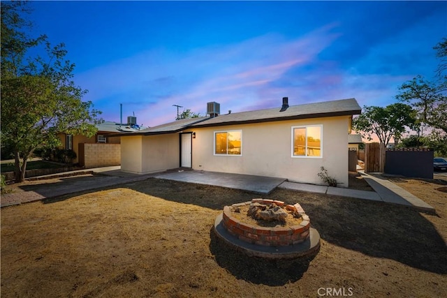 back of house at dusk featuring an outdoor fire pit, fence, a patio area, and stucco siding