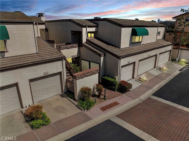view of property featuring a garage, stucco siding, driveway, and a tiled roof
