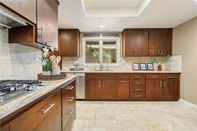 kitchen with a raised ceiling, ventilation hood, a sink, appliances with stainless steel finishes, and backsplash