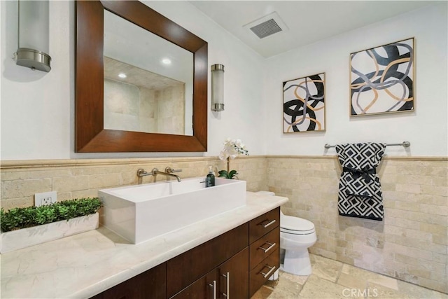 bathroom with wainscoting, vanity, toilet, tile walls, and visible vents