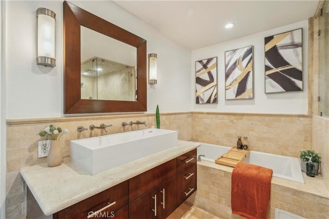 full bathroom with tile walls, wainscoting, a bath, and vanity
