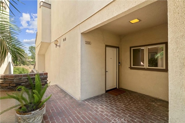view of exterior entry with stucco siding and a patio area